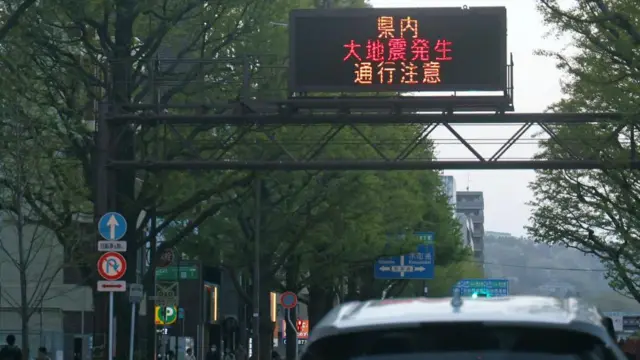 A car drives underneath a digital sign with a warning written on it in Japanese