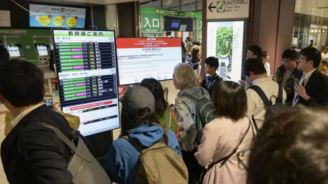 A group of apssengers look at information boards in a Japanese railway station.