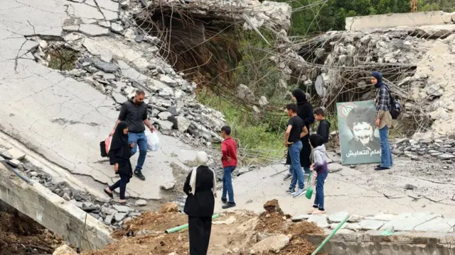 Nine displaced people, including women and children, walk across a destroyed bridge