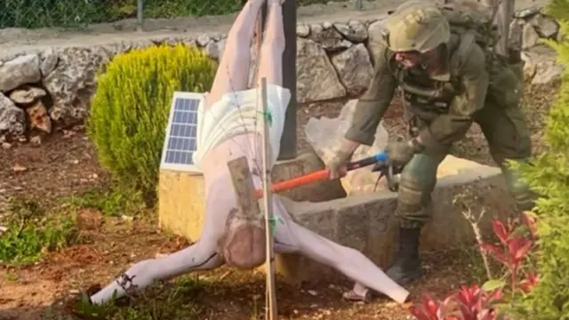 Imagem mostrando um soldado golpeando uma estátua caída de Jesus Cristo com uma marreta.