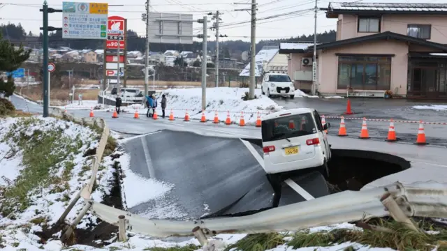 A white car balances across a hole in the rode following an earthquake.
