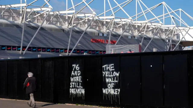 A Southampton fan walks to St Mary's in front of graffiti related to Southampton's 1976 FA Cup win