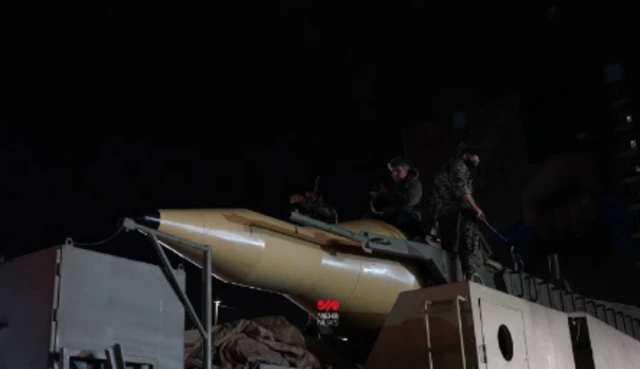 Close up of a cream-coloured missile with three uniformed officers around it