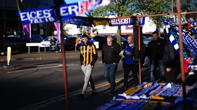 Hull and Leicester fans walk past a stall selling scarves outside the King Power Stadium