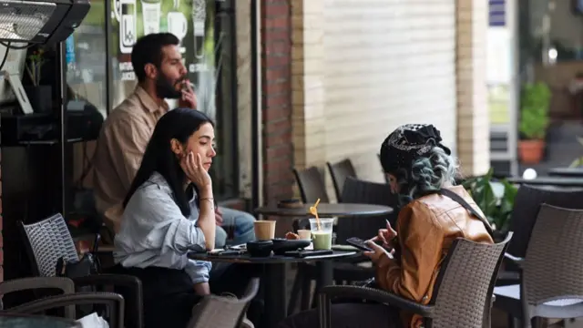 Two women sit at a cafe table with drinks in Tehran on April 21, 2026, amid a ceasefire in the region