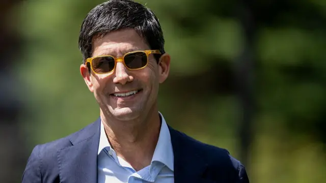 Kevin Warsh wears orange sunglasses, a dark suit and a white shirt