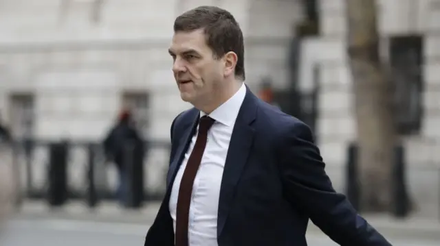 Olly Robbins is seen walking in Westminster, wearing a dark suit and dark red tie.
