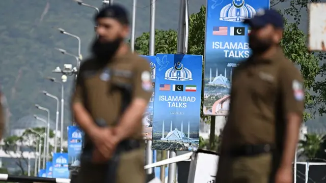 Two security guards stand in front of lamp posts with posters reading Islamabad talks