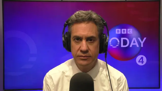 Ed Miliband sits behind a microphone with with the BBC Radio 4's Today programme graphic behind him. He is wearing a white shirt and headphones.