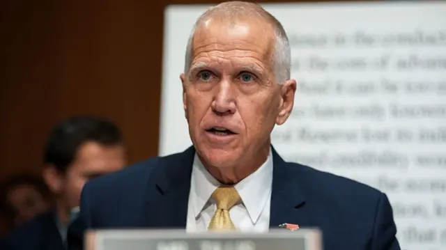 Tillis sits on the dais in the US Senate. He wears a dark suit and gold tie