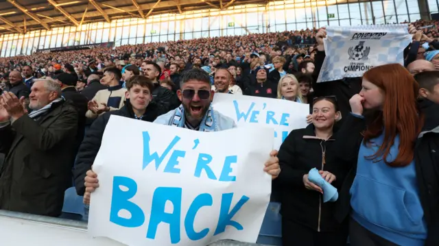 Coventry fans celebrate with a banner reading "We're back"