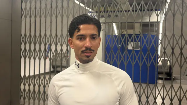 Headshot of South, who stands in front of a barrier blocking off two escalators