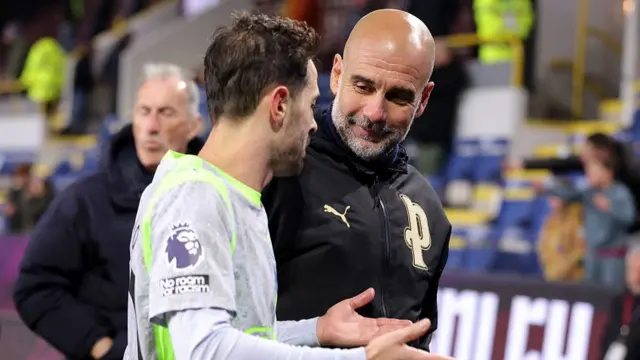 Pep Guardiola, Manager of Manchester City, speaks with Bernardo Silva