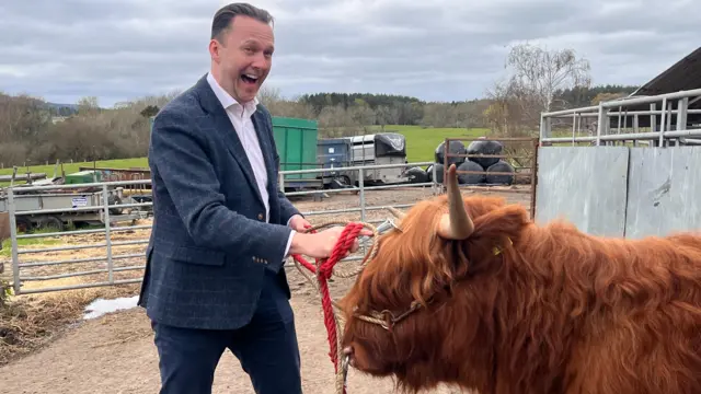 Russell Findlay standing next to a Highland cow on a farm