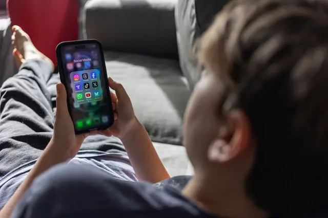 A boy lying on the sofa and looking at the apps on his phone
