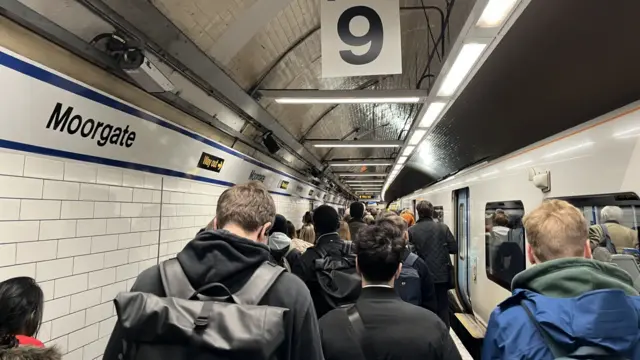 People walking along a busy train platform beside a train in Moorgate