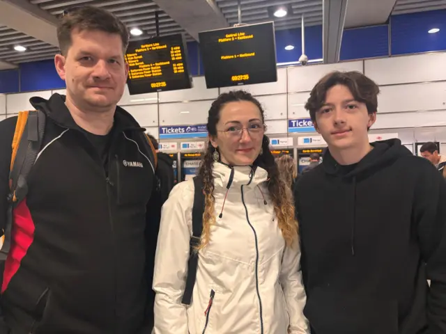 A young man with a black jacket, a young woman with glasses and long brown hair and a young man with floppy dark hair, wearing a black hoodie