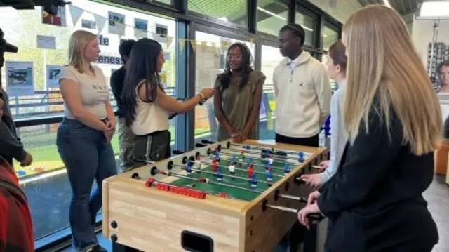 A group of young people being interviewed around a foosball table.