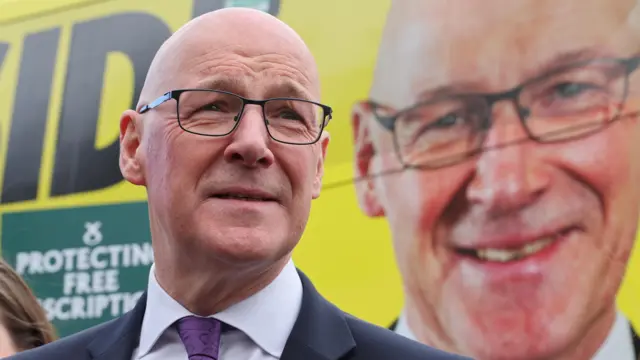 John Swinney standing in front of the SNP's campaign bus, which has his face on the side