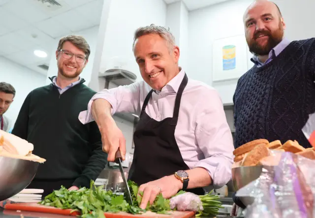 Alex Cole-Hamilton chopping salad in a kitchen, standing between two other men.