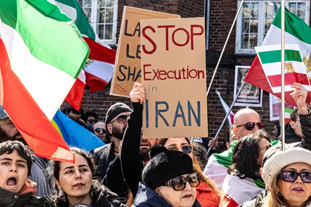 A group of protesters holding Iranian flags and placards. A placard in the foreground reads: "Stop execution in Iran".