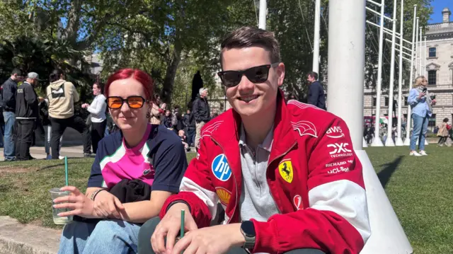 Dylan wears a red Ferrari jacket and sits next to a friend in orange glasses and a pink and blue top