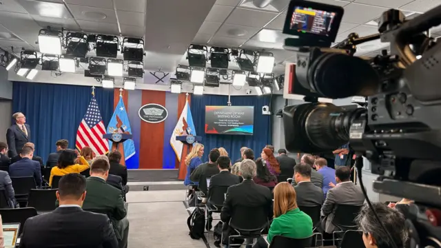Pentagon room with several reporters. There are two podiums and an American flag