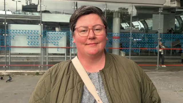 A woman wearing glasses and a green jacket over a grey top