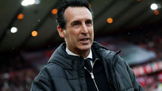 Unai Emery in a black coat and suit with the stadium in backdrop