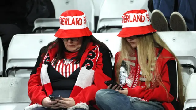 Fans sit on their phone surrounded by empty seats