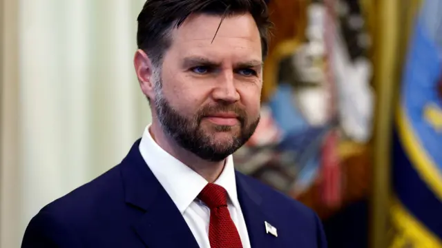 US Vice President JD Vance in a blue suit, white shirt and red tie while standing in the Oval Office