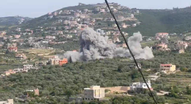A screengrab from a video of a large smoke cloud rising over a village