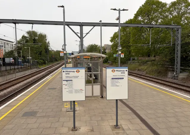 The platform at Caledonian and Barnsbury Overground station which has a few people sitting under a shelter
