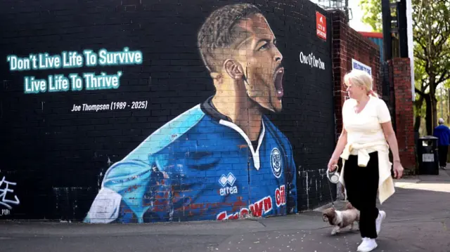 A woman walking her dog walks past a mural to former Rochdale midfielder Joe Thompson bearing the message: "Don't live life to survive, live life to thrive"