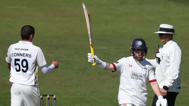 Marcus Harris raises his bat as Sam Conners looks on