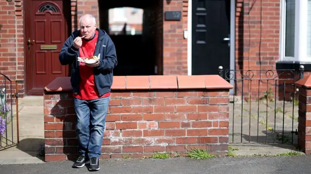 A York City fans eats chips while perched on a wall