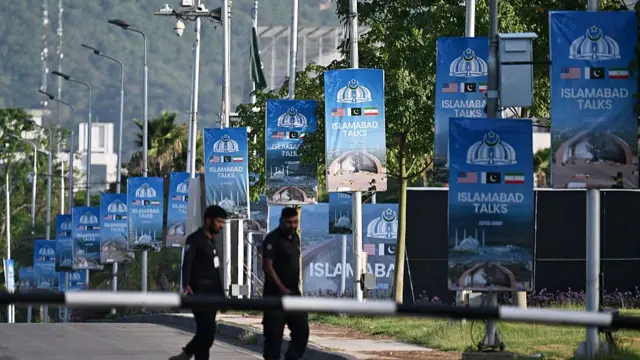 Two men walk on the road, past posters reading 'Islamabad talks'