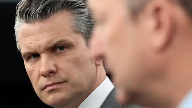 Pete Hegseth pictured close up, in the foreground is the blurred side profile of Dan Caine