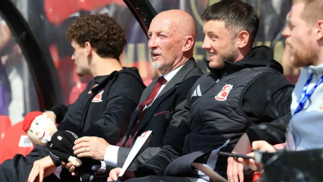 Ian Holloway, manager of Swindon Town holds a knitted effigy of himself as he sits in the away team dugouts ahead of their EFL League Two match against Grimsby Town.