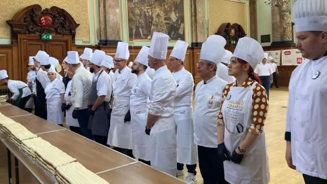 A line of chefs stand behind a long dessert on a table