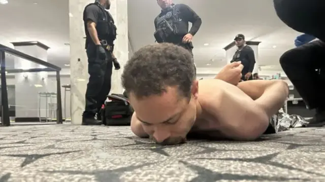 Man being detained, as he lies down with arms behind his back