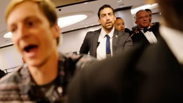 Robert F. Kennedy Jr. (right) wearing a bow-tie is escorted out of the venue by security.