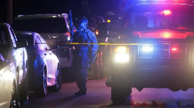 Police stand by cars behind a cordon