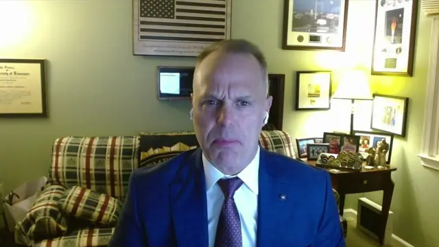 Former FBI special agent Jeff Kroeger speaks to BBC Breakfast. He's wearing a dark blue suit, white shirt and tie while sitting in what appears to be an office in a private hope, a chequered couch and family pictures on a wooden table behind him