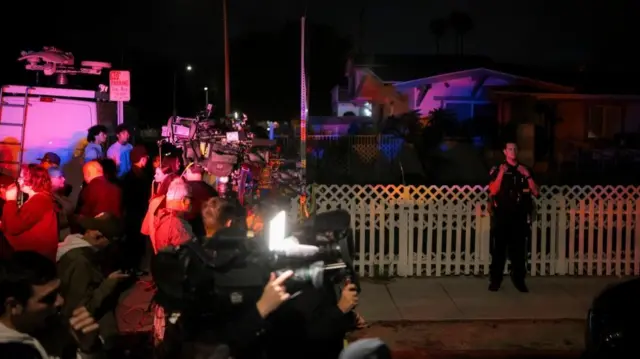 Journalists stand by a white fence