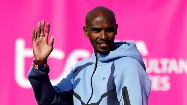 Sir Mo Farah wearing a light blue Nike tracksuit top waves.