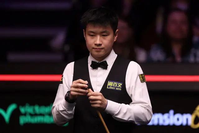 Zhao Xintong of China chalks the cue