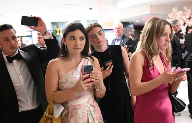 Attendees check their phones in the lobby of the Washington Hilton after shots were heard during the White House Correspondents' Dinner in Washington