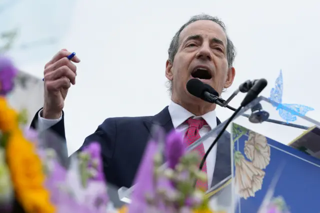 Congressman Jamie Rankin mid-speech in front of a mic and lectern set up outdoors