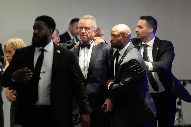 Law enforcement officers surround Robert F Kennedy Jr., US secretary of Health and Human Services (HHS), and his wife, actress Cheryl Hines following reports of a shooting during the White House Correspondents' Association (WHCA) dinner in Washington, DC, US on Saturday, April 25